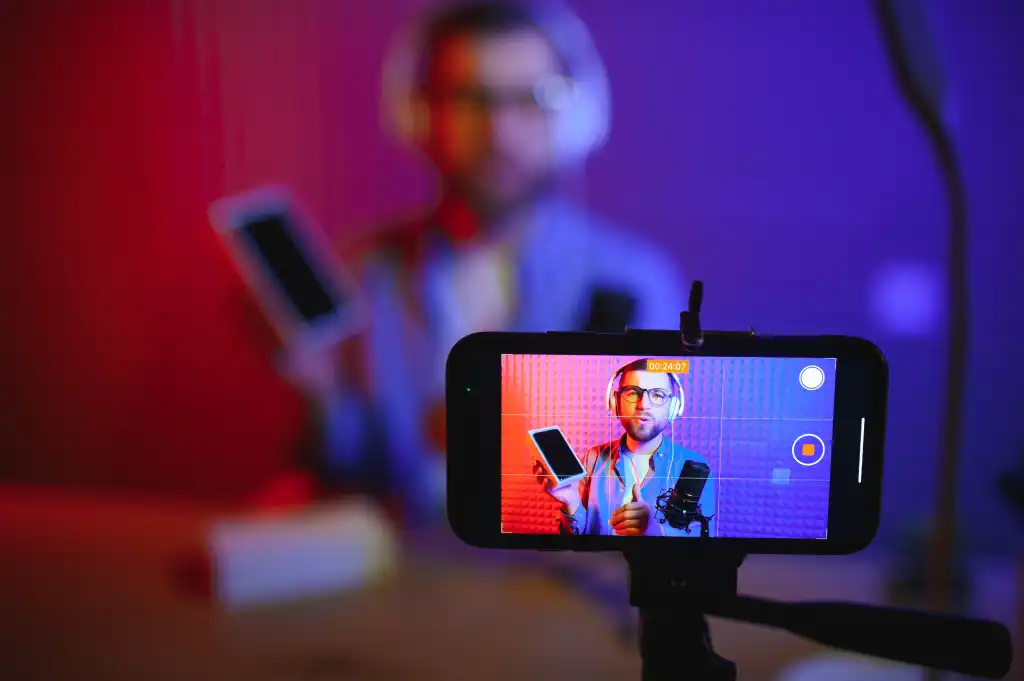 Ein männlicher Tech-Blogger zeichnet einen Video-Blog oder eine Vlog-Rezension über ein neues Smartphone auf, das es vorführt