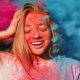positive blonde woman having fun with exploding blue pink dry powder celebrating holi festival